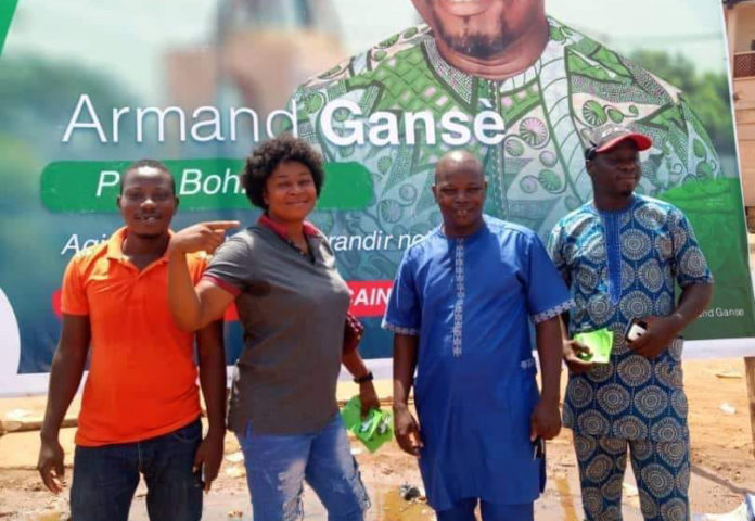 Des électeurs posant devant l'affiche d'un candidat dans la ville de Bohicon. © Ahinadjê Baba Assan